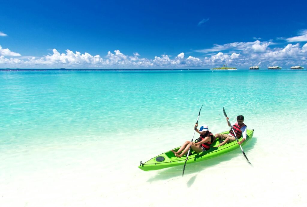 Two people kayaking in clear turquoise waters on a sunny tropical beach.