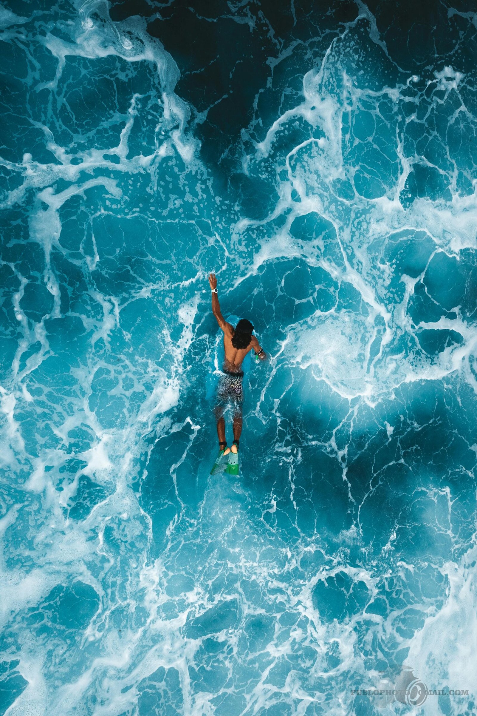 Aerial photo of surfer navigating bright blue ocean waves in Fuvahmulah, Maldives.